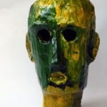 Papiermaché-Kopfskulptur in Grün-Gelb mit schwarzen Augen- und Mundöffnungen | Papier-mâché head sculpture in green and yellow with black eye and mouth openings