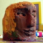 Tonkopf-Skulptur mit langen Haaren, dunkelrot bemalt, im Atelier | Clay head sculpture with long hair, painted dark red, in artist's studio