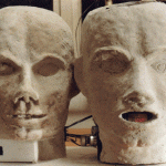 Zwei Gipsköpfe: links skelettartig, rechts mit digitalem Display im Mund | Two plaster heads: left skull-like, right with digital display in mouth