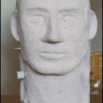 Gipsabguss eines männlichen Kopfes mit vereinfachten Gesichtszügen auf rundem Sockel | Plaster cast of a male head with simplified facial features on a round base