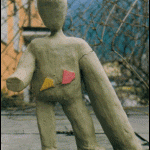 Grobe Tonskulptur einer menschlichen Figur mit bunten Dreiecken auf dem Torso | Rough clay sculpture of a human figure with colorful triangles on the torso