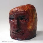 Expressiver Tonkopf in Dunkelrot mit orangefarbenen Farbspuren, grob modelliert | Expressive clay head in dark red with orange paint traces, roughly modeled