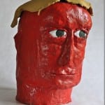 Rot bemalter Pappmaché-Kopf mit gelbem Haar und grünen Augen | Red painted papier-mâché head with yellow hair and green eyes
