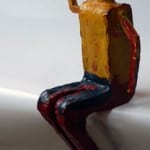 Bemalte Holzfigur einer sitzenden Person mit gelbem Oberteil und dunkler Hose | Painted wooden figure of a sitting person wearing yellow top and dark trousers