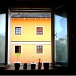 Geöffnetes Fenster mit vier Pflanzentöpfen, Blick auf orangefarbenes Gebäude | Open window with four plant pots, view of orange building facade