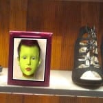 Regal mit pinkem Rahmen, gelbgrünem Kinderkopf-Kunstdruck und schwarzem Sandalette | Shelf with pink frame, yellow-green child head art print and black sandal heel