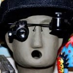 Grauer Keramikkopf mit schwarzem Hut und Uhrmacherlupe, offener Mund | Grey ceramic head with black hat and watchmaker's loupe, open mouth