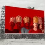 Digitale Collage: Fünf Figuren mit goldenen Kronen auf rotem Billboard in grauer Industrielandschaft | Digital collage: Five crowned figures on red billboard amid grey industrial wasteland