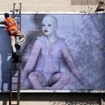 Arbeiter auf Leiter klebt großes Billboard mit kahlköpfiger Puppenfigur in Bodysuit | Worker on ladder installing large billboard featuring bald doll-like figure in bodysuit
