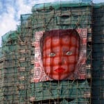 Riesiges rotes Gesicht mit blauen Augen als Banner an grünem Baugerüst | Huge red face with blue eyes as banner on green scaffolding