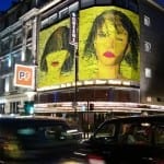 Zwei gelb-schwarze Porträts auf beleuchtetem Queens Theatre London bei Nacht | Two yellow-black portraits on illuminated Queen's Theatre London at night