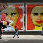 Großformatige Street-Art-Plakate mit stilisierten Gesichtern in Gelb-Rot, Passanten davor | Large-scale street art posters with stylized faces in yellow-red, pedestrians in front