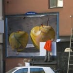 Mann in Orange klebt riesiges Plakat mit zwei gelben Äpfeln an Hausfassade | Man in orange jacket pastes large billboard with two yellow apples on building facade