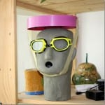 Betonkopfskulptur mit gelber Schwimmbrille und pinkfarbenem Sonnenschutz-Visier | Concrete head sculpture wearing yellow swim goggles and a pink sun visor