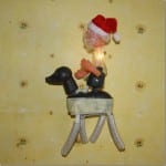 Weihnachtsmann-Figur mit Zipfelmütze reitet auf schwarzem Hund, leuchtend | Santa Claus figure with red hat riding black dog toy, glowing light inside