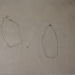 Zwei gebogene Drahtformen an weißer Wand befestigt | Two bent wire shapes attached to a white wall