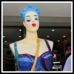 Schaufensterpuppe mit blauem Haar, rotem Mund, buntem Kleid und gelber Umhängetasche | Mannequin with blue hair, red lips, colorful dress and yellow shoulder bag