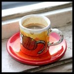 Espressotasse mit Katzen-Motiv in Orange-Rot auf passendem Unterteller am Fensterbrett | Espresso cup with cat motif in orange-red on matching saucer on windowsill