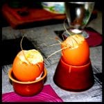 Zwei aufgeschlagene Eier in braunen Eierbecher mit Strohhalm-Dekoration auf gedecktem Tisch | Two cracked eggs in brown egg cups with straw decoration on a set table