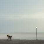 Minimalistisch: Sessel und leuchtende Stehlampe am nebligen Meeresufer | Minimalist: armchair and glowing floor lamp on misty shoreline
