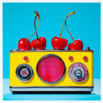 Gelbes Retro-Radio mit rotem Lautsprecher, vier rote Kirschen obenauf, türkiser Hintergrund | Yellow retro radio with red speaker, four red cherries on top, turquoise background