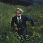 Blonder junger Mann im Anzug rennt panisch durch hohes grünes Gras | Blond young man in suit running frantically through tall green grass