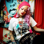 Frau mit pinkem Haar, Kopftuch, Tattoos und Schmuck vor buntem Pop-Art-Hintergrund | Woman with pink hair, headscarf, tattoos and jewelry against colorful pop art background