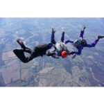 Vier Fallschirmspringer im freien Fall über grüner Landschaft, Helmformation | Four skydivers in freefall formation over green rural landscape, wearing helmets