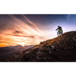 Mountainbiker fährt steilen Berghang hinab, dramatischer Sonnenuntergang | Mountain biker descending steep rocky slope against dramatic sunset sky