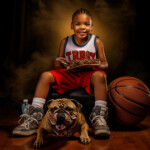 Junge im Basketball-Trikot sitzt mit Bulldogge, Ball und Teller vor dunklem Hintergrund | Boy in basketball jersey sits with bulldog, ball and plate against dark background
