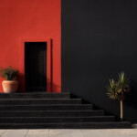 Rote Hausfassade mit schwarzer Tür, dunkle Treppe, Yucca und Tontopf | Red building facade with black door, dark stairs, yucca plant and terracotta pot